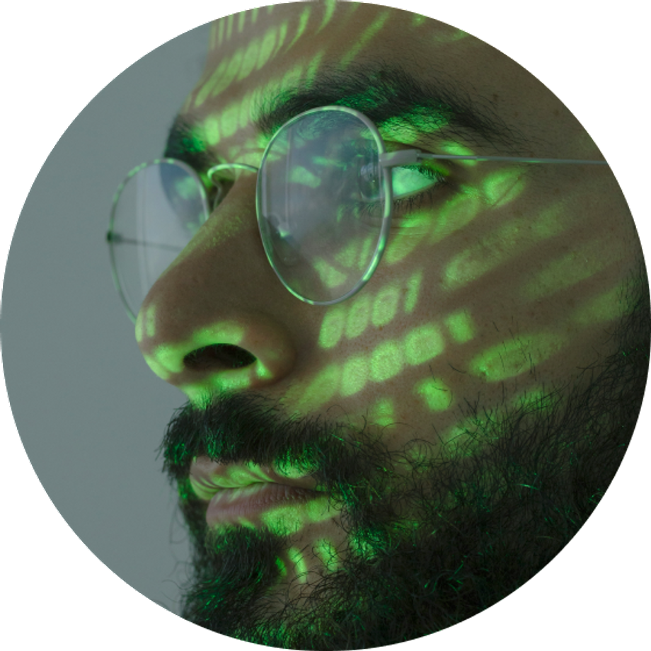 A bearded man with round glasses and green lights projected on his face