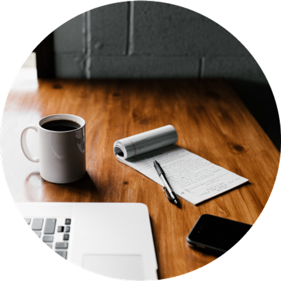 Mug, computer, notepad and cellphone on top of a wooden table