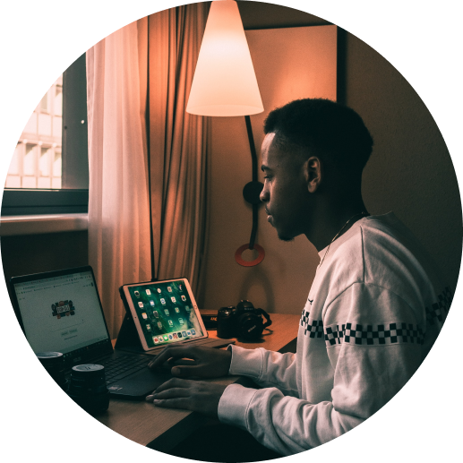 Black man using his laptop and tablet with a low-lit lamp