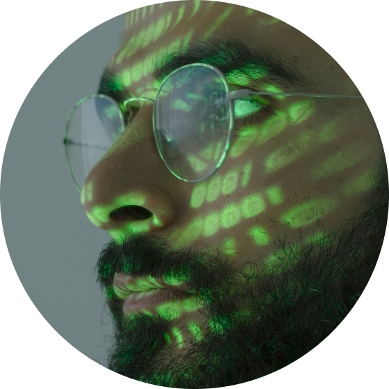A bearded man with round glasses and green lights projected on his face